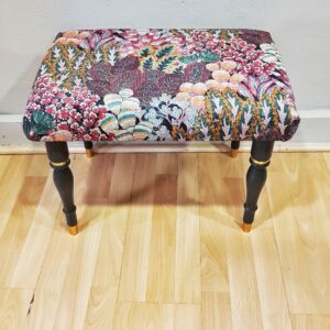 Banqueta tapizada vintage con estampado floral y patas negras con dorado.