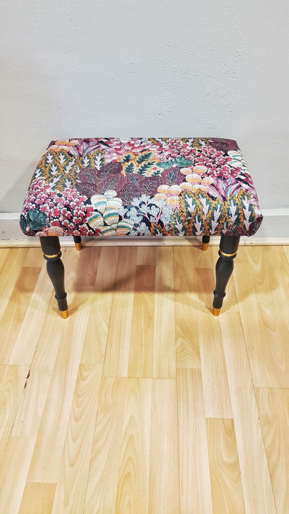 Banqueta tapizada vintage con estampado floral y patas negras con dorado.