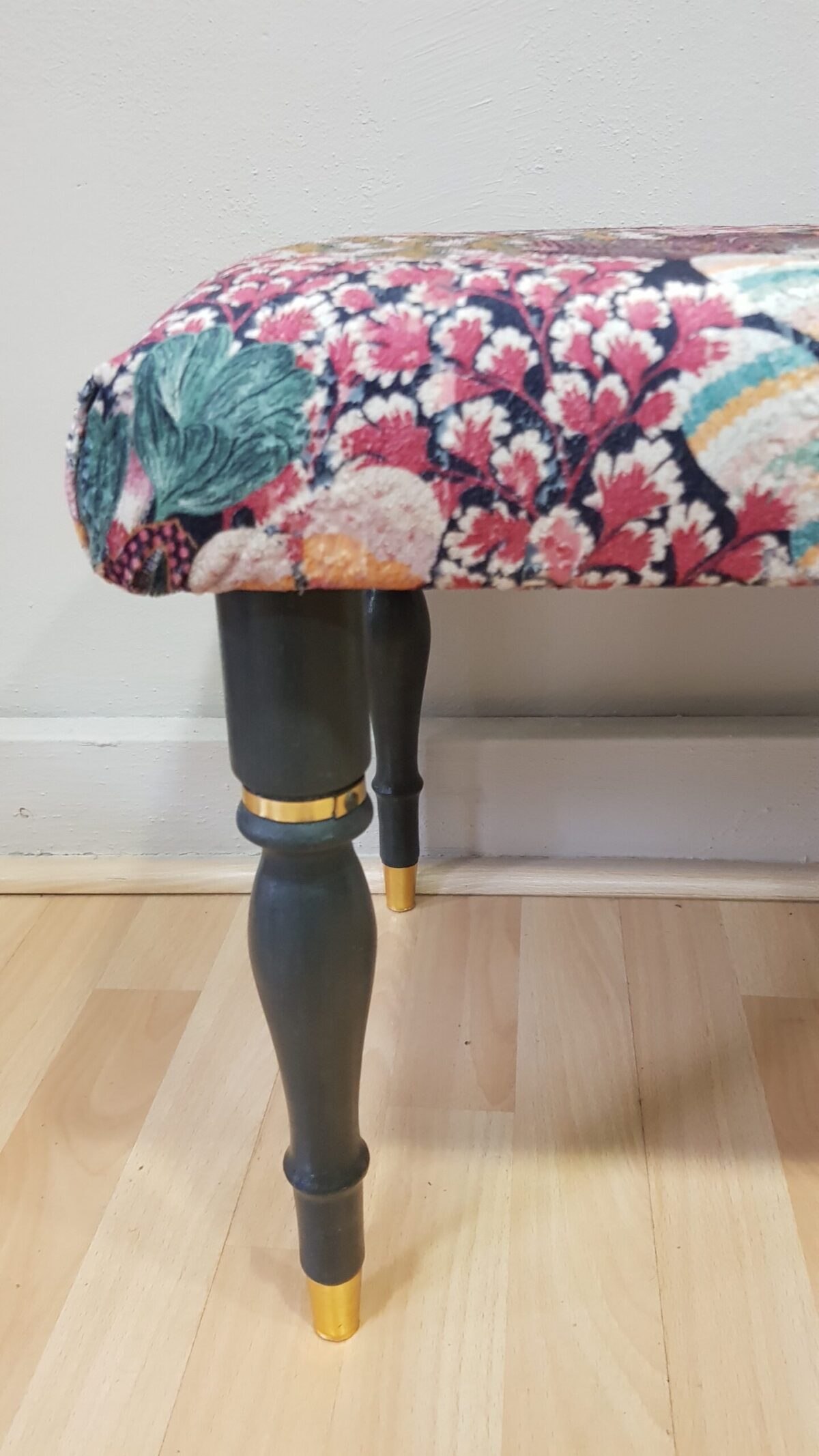 Banqueta tapizada vintage con estampado floral y patas negras con dorado.