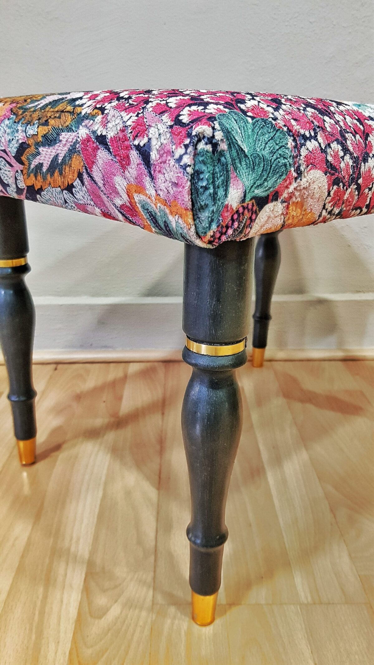 Banqueta tapizada vintage con estampado floral y patas negras con dorado.