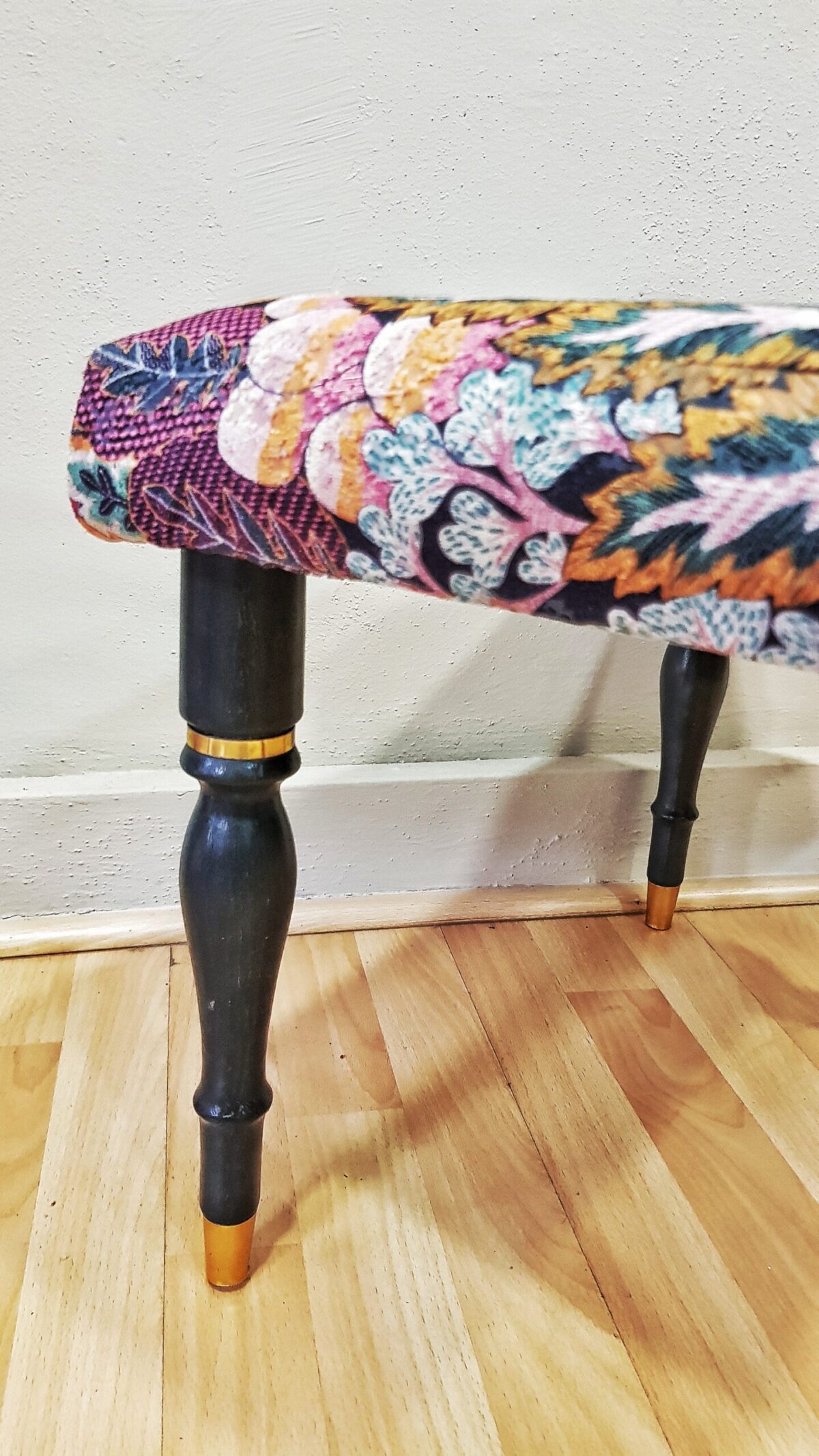 Banqueta tapizada vintage con estampado floral y patas negras con dorado.
