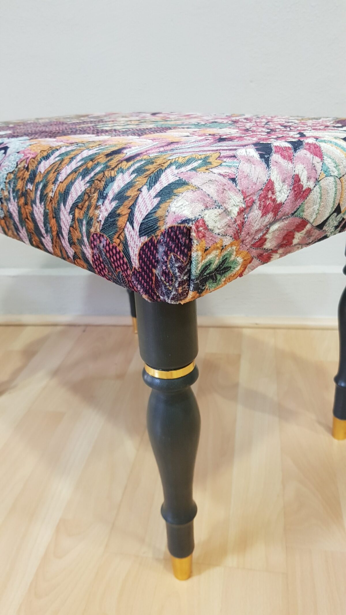 Banqueta tapizada vintage con estampado floral y patas negras con dorado.