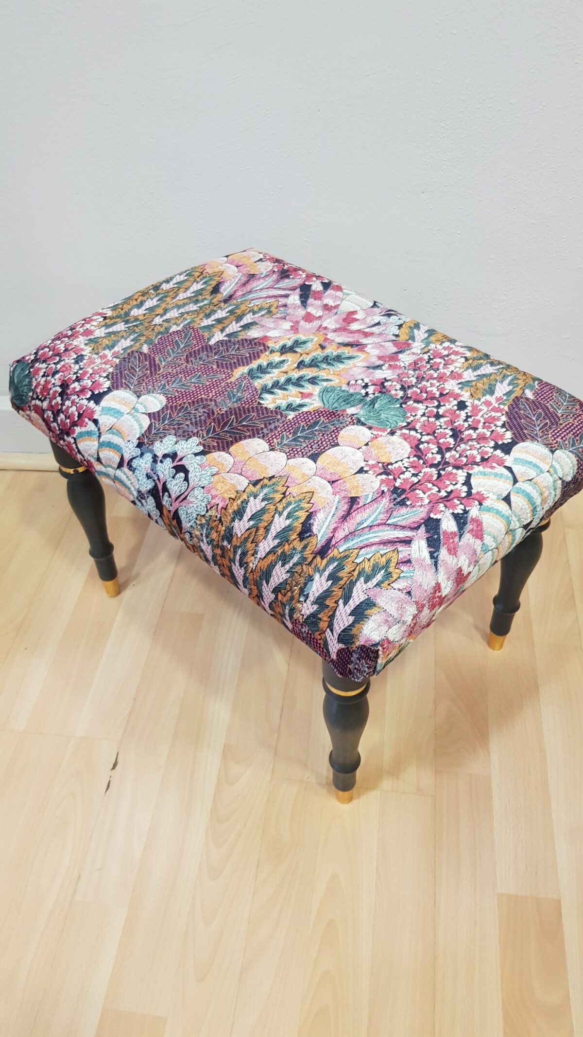 Banqueta tapizada vintage con estampado floral y patas negras con dorado.