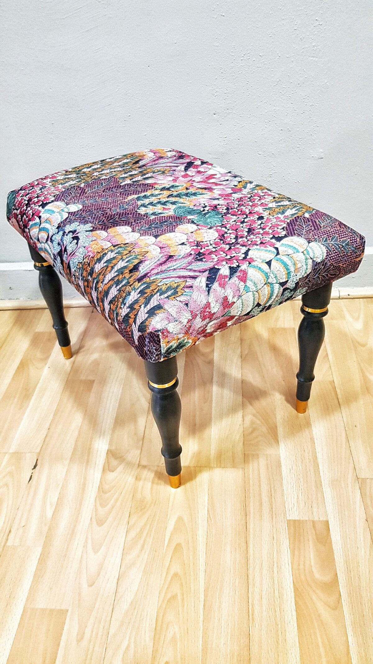 Banqueta tapizada vintage con estampado floral y patas negras con dorado.